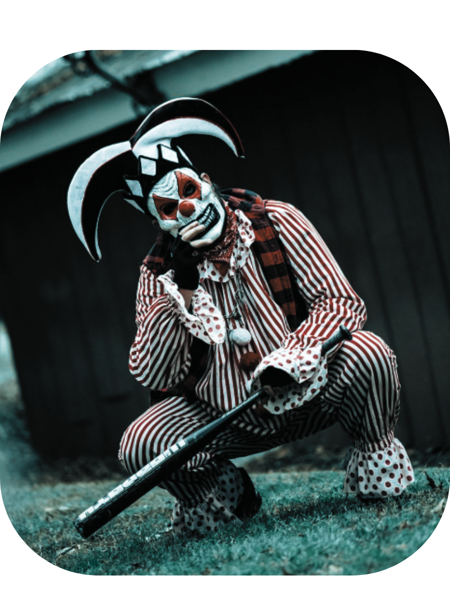 Jester: a masked jester in a black-and-white striped suit and horned hood, crouched with a bat.