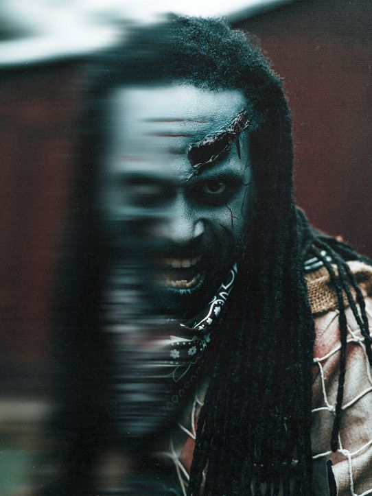 Schizo: a motion-blurred portrait of a dreadlocked figure with a scarred face and manic grin.